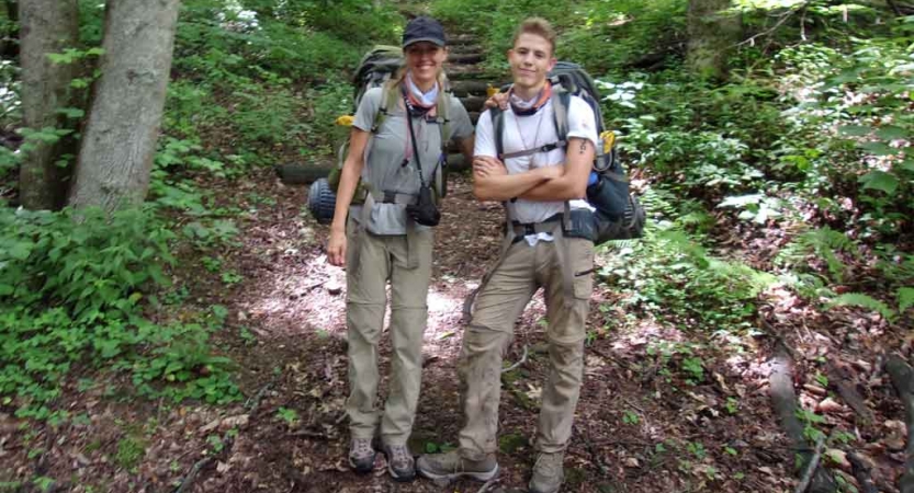 a parent and their child are wearing backpacking gear while smiling at the camera on an outward bound course in north carolina